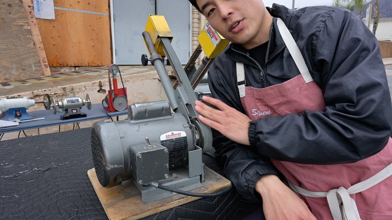 Steven from Outdoors55 presenting a Kalamazoo industrial 1x42 belt grinder on a wood pallet — professional knife sharpening equipment